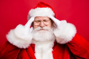 Annoyed depressed disappointed displeased frowning frustration grumpy stylish aged grandfather Santa face with grimace and close eyes hold white hands on head isolated on shine red background
