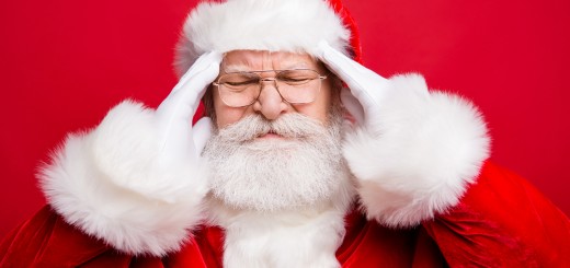 Annoyed depressed disappointed displeased frowning frustration grumpy stylish aged grandfather Santa face with grimace and close eyes hold white hands on head isolated on shine red background